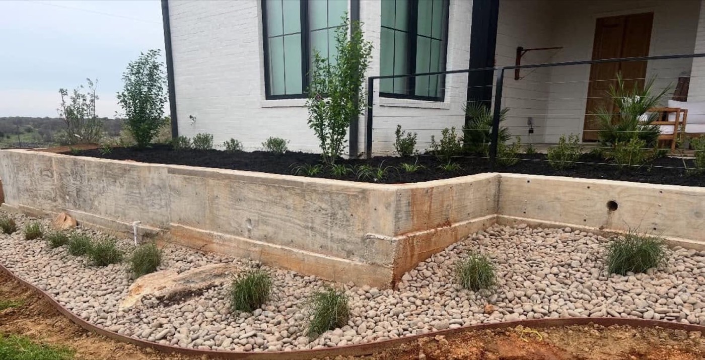 Raised stone landscape bed filled with river rock and grasses